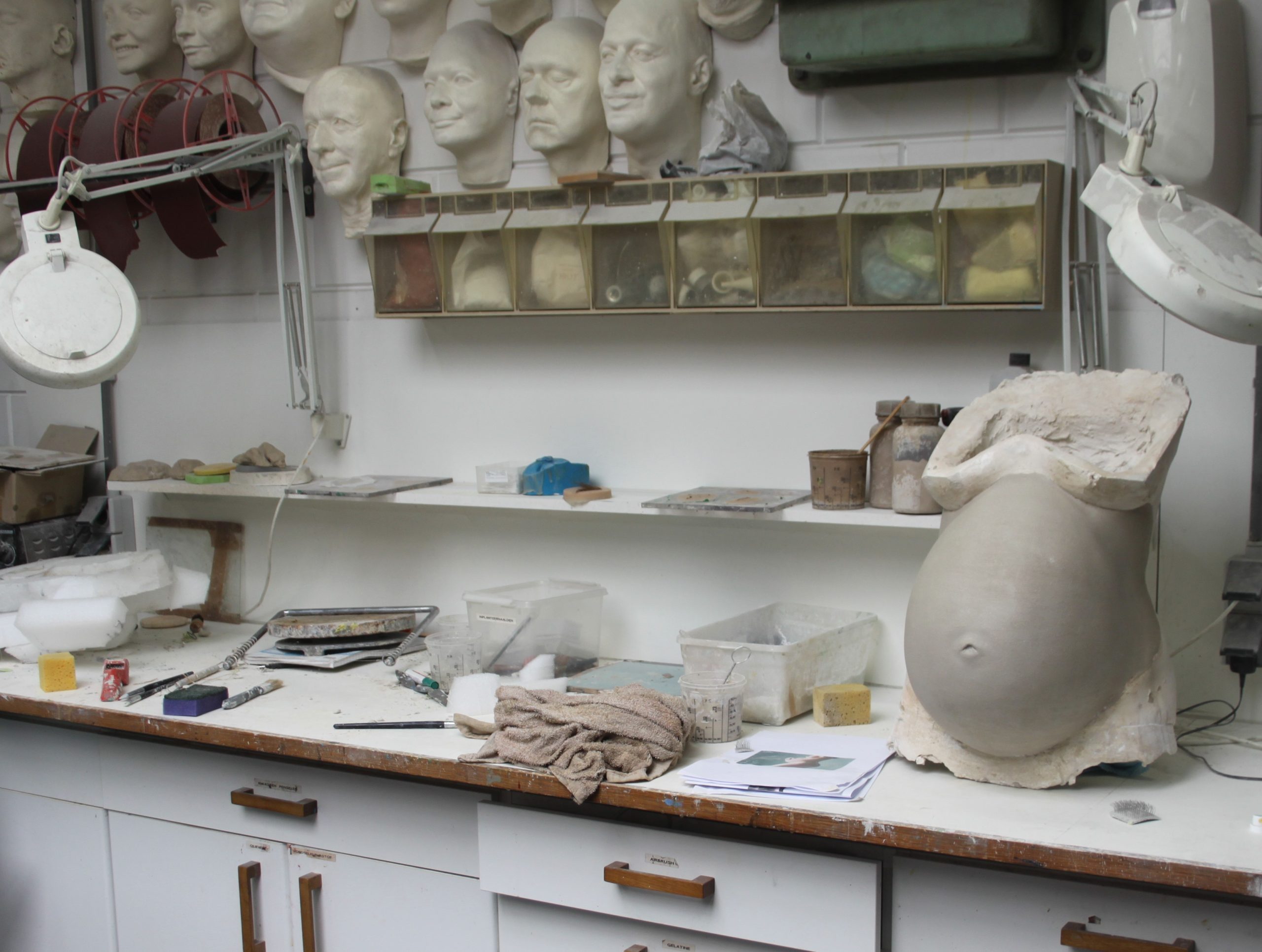 Interieur van Robspropshop met op de achtergrond, gipshoofden die zijn afgedrukt en op de voorgrond een zwangerschapsbuik die gesculpteerd word.