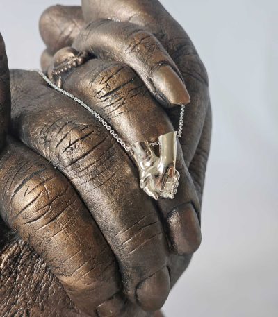 Gedenksieraad met handen afgedrukt in bronskleur plus bedel in zilver van het zelfde beeld